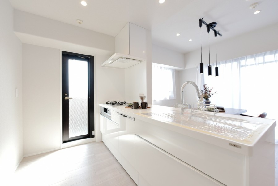 バルコニーへとつながる勝手口が付いたキッチンです。対面式のオープンキッチンで開放感があり、ホワイトで統一感のある清潔感溢れる空間です。食器洗浄乾燥機も完備で家事の時短にお役立て下さい。