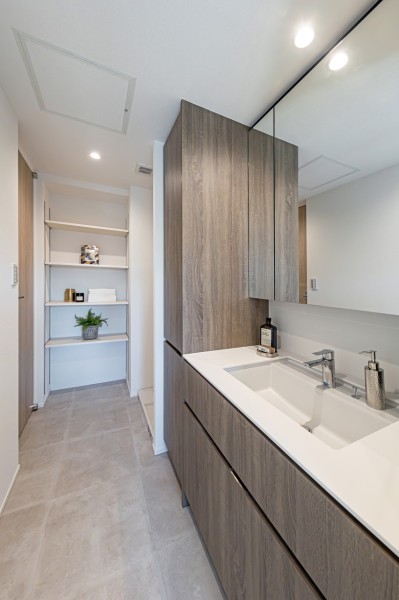 洗面化粧台は、キッチンと同じく田中工藝製で上品さが宿ります。洗濯機置場の上には便利な吊戸棚を備え、リネン類などの収納に便利な可動棚も備え付けています。