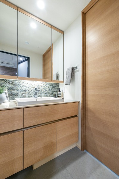 空間に美しく溶け込むスタイリッシュなデザインの洗面化粧台は、収納豊富な三面鏡タイプです。タイルがアクセントとして設置されています。