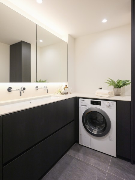 モノトーンカラーの洗面室は、ホテルライクなダブル水栓タイプの洗面化粧台を設置いたしました。三面鏡裏と足元に収納棚を造作し、お部屋を広くご使用いただけます。ミーレ製の洗濯機を設置しております。