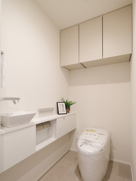 手洗いカウンターを備えたトイレスペースです。上部収納付きで日用品の整理にも配慮されており、白を基調とした明るく清潔感のある印象に仕上げました。