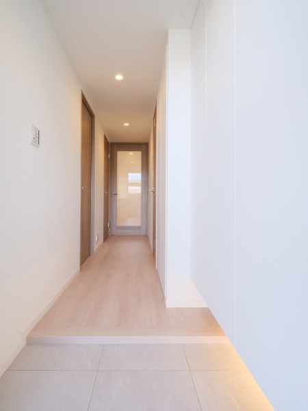 明るい木目の建具とフローリングが調和する廊下です。正面の採光ドアが視線を先まで通し、空間に軽やかな印象を与えています。
