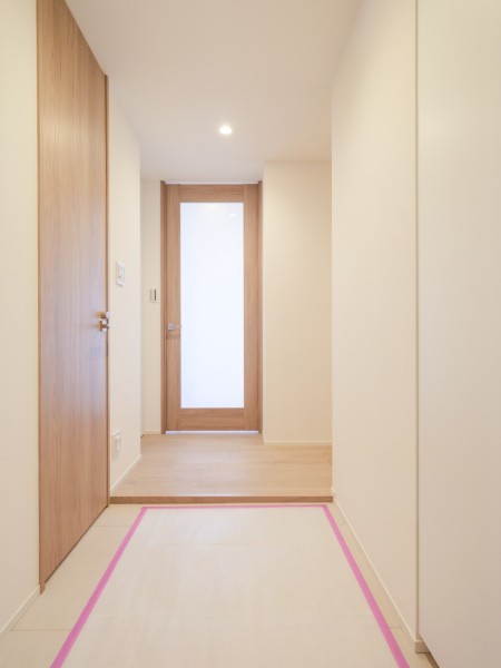 明るい木目の建具とフローリングが調和する廊下です。正面の採光ドアが視線を先まで通し、空間に軽やかな印象を与えています。