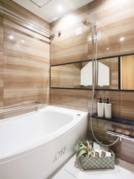 光沢のある木目調パネルが高級感を漂わせるバスルームです。ワイドミラーによって実際より広く感じられるくつろぎの空間です。