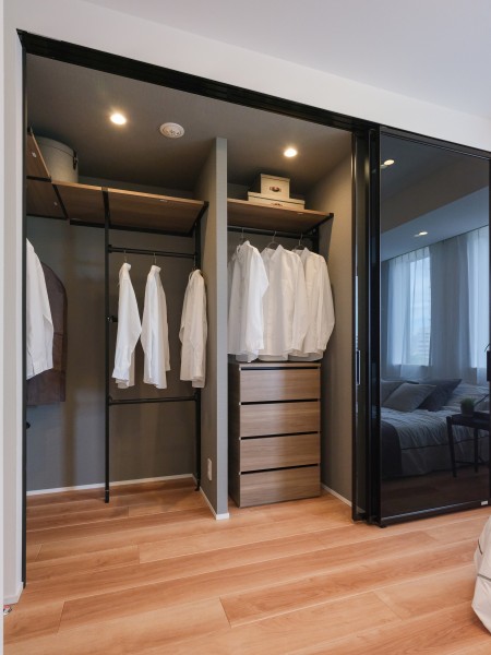 洋室1には、約1.8帖のウォークインクローゼットがありお洋服や小物、季節物の寝具など収納することができます。スモーク調のガラス扉で、スタイリッシュな空間となっております。扉を開放することでお洋服を眺めることができ、扉を閉めても程よい距離感のシームレスな空間が生まれます。