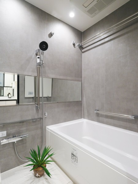 横長ミラーの効果で実際のサイズよりも広がりを感じるバスルームです。グレー調のタイルが洗練さを纏う、落ち着きのある空間です。