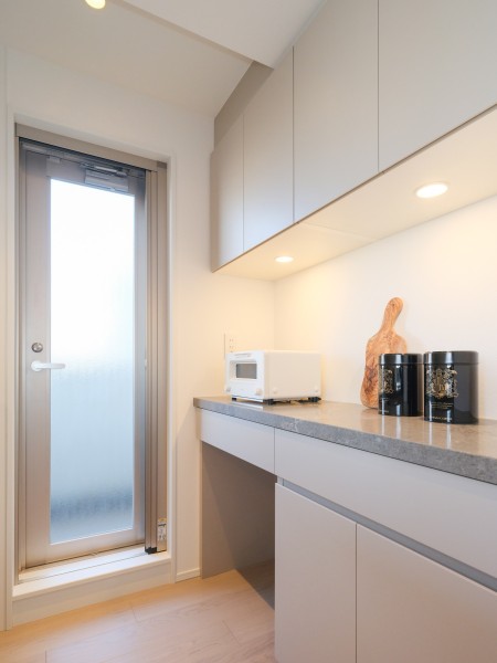 キッチン背面には、デザインを統一した機能的なカップボードを配置しました。食器や調味料がスマートに収まる設計です。棚下灯の光がアクセントとなり、日々使う調理家電やこだわりの雑貨をより魅力的に演出します。