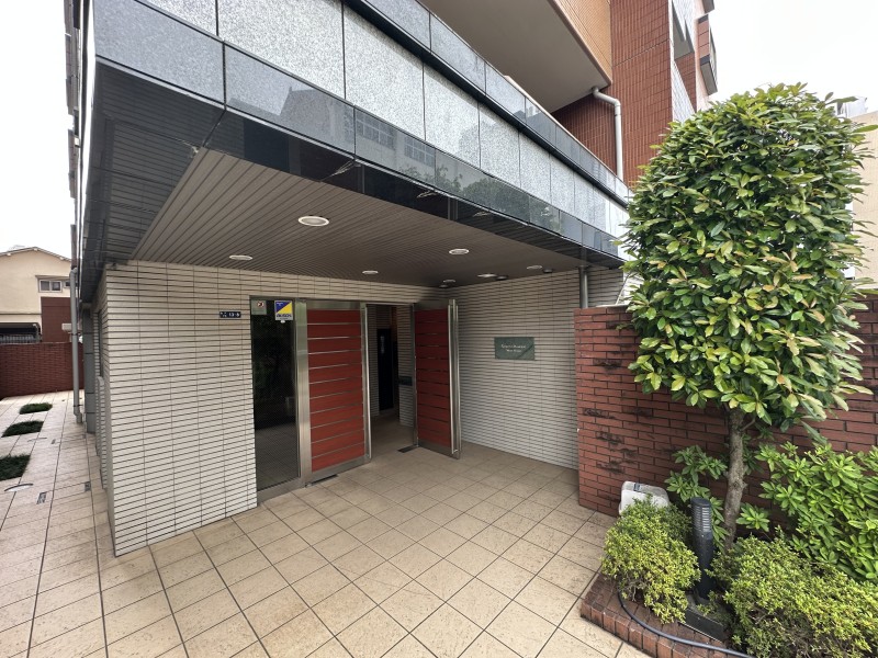 重厚感あふれるタイル貼りのアプローチが印象的なエントランスです。緑豊かな植栽が彩りを添え、マンションの顔にふさわしい気品ある雰囲気を演出しています。