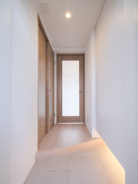明るい木目の建具とフローリングが調和するホール部分です。正面の採光ドアが視線を先まで通し、空間に軽やかな印象を与えています。